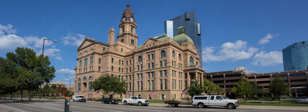 Historic stone government building with clock tower and green dome, lined by American flags on a city street.