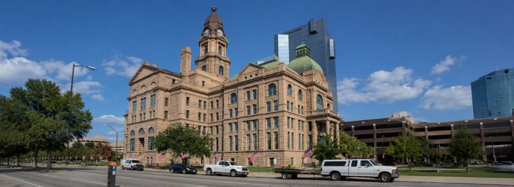 Historic stone government building with clock tower and green dome, lined by American flags on a city street.
